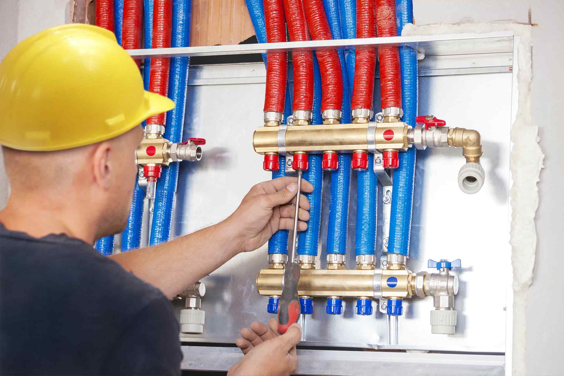 gallery_projects_18 Technician using a screwdriver to adjust plumbing connections with red and blue hoses, highlighting Central Plumbing, Heating & Air Conditioning's expertise in reliable plumbing solutions.