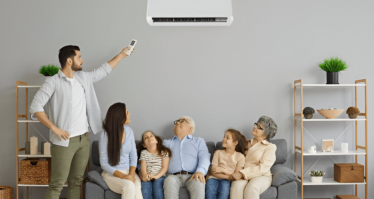Family enjoying cool air from a modern wall-mounted AC unit, with a man using a remote control, in a cozy living room setting, emphasizing HVAC comfort solutions.